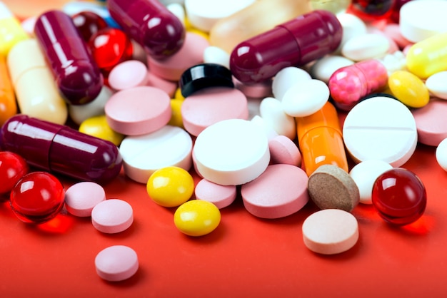 Colorful pills and capsules on red surface