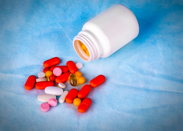 Colorful pills of medicine from a plastic drug bottle on blue