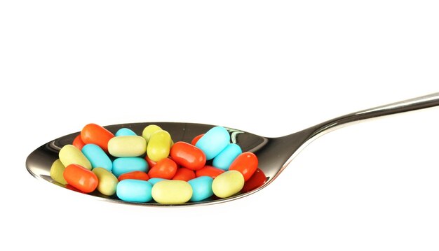 Colorful pills on spoon on white background closeup