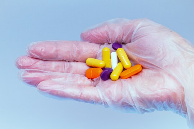 Colorful pills, tablets in hand in a medical glove. Drug protection, treatment of viruses, antiviral, diseases concept.