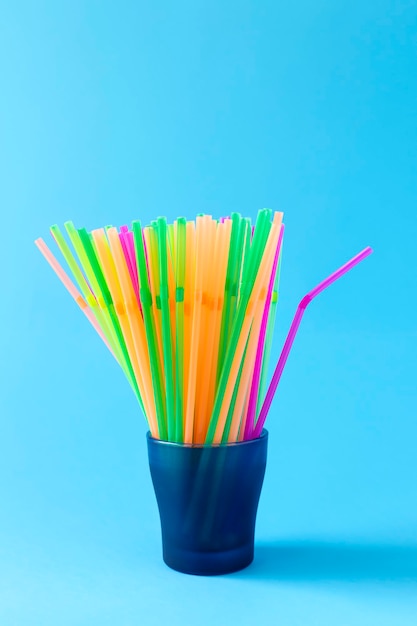 Colorful plastic drinking straws in glass container on light blue