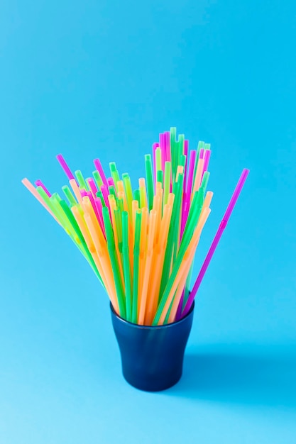 Colorful plastic drinking straws in glass container on light blue