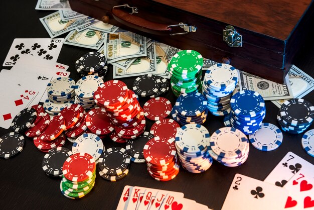 暗い背景にトランプとアメリカのドルを持つカラフルなポーカー チップ。