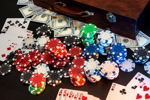 Colorful poker chips with playing cards and american dollars on dark background.