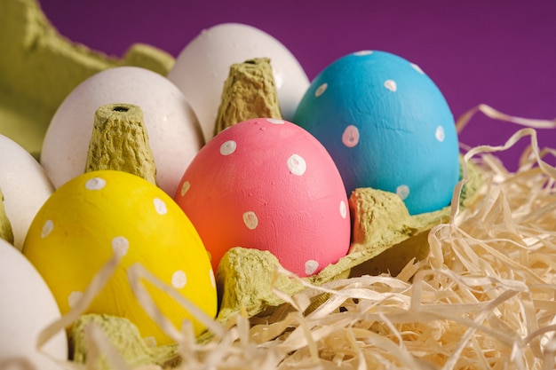 Фото Красочные пасхальные яйца в горошек в лотке для яиц на деревянном гнезде на фиолетовый фиолетовый