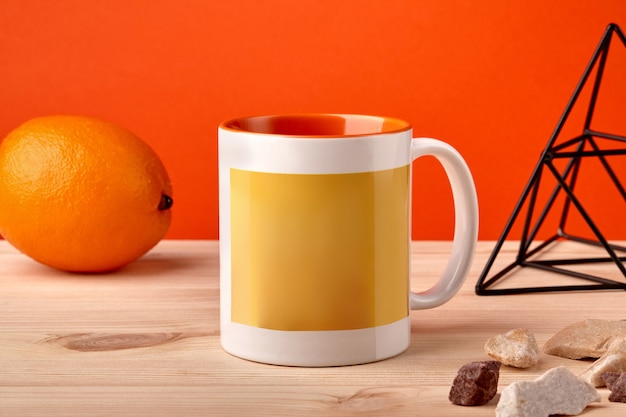 Colorful porcelain mug on wooden desktop next to orange