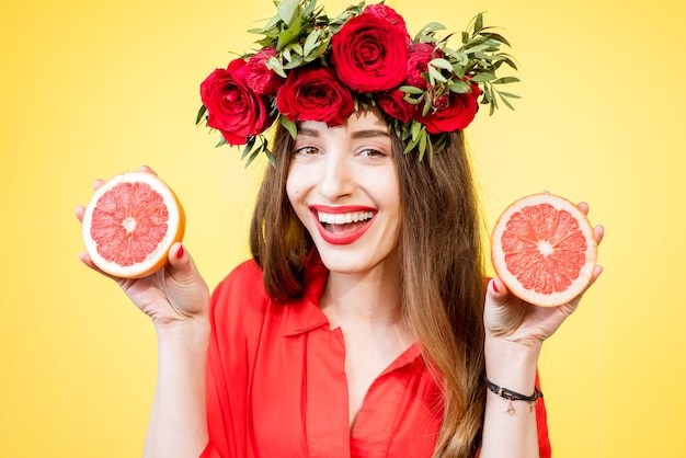 Colorful portrait of a beautiful woman with flower wreath holding slices of grapefruits on the yellow background