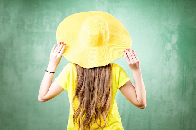 Colorful portrait of a beautiful woman in yellow t-shirt and hat on the green background. Back view