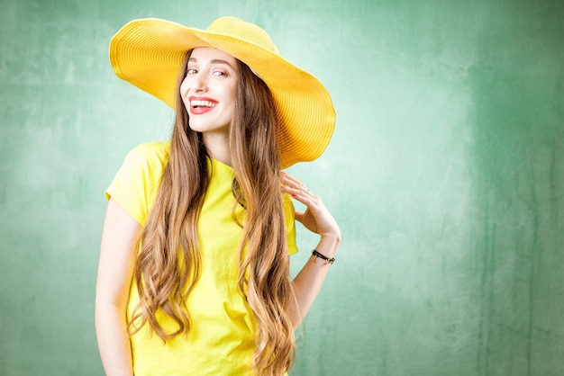 Colorful portrait of a beautiful woman in yellow t-shirt and hat on the green background