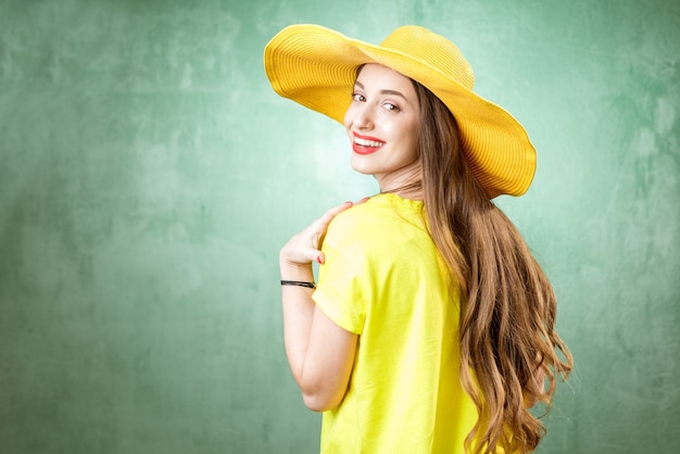 Красочный портрет красивой женщины в желтой футболке и шляпе на зеленом фоне