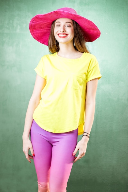 Colorful portrait of a beautiful woman in yellow t-shirt and pink hat on the green background