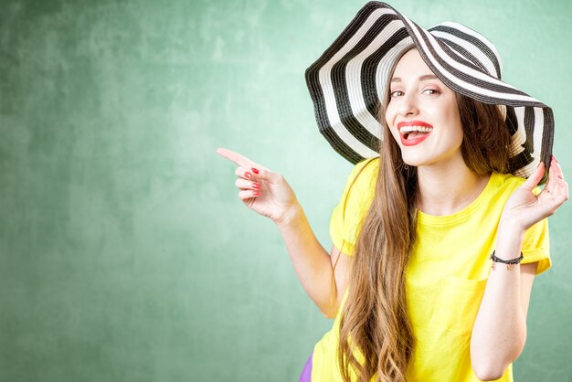 Foto ritratto colorato di una bella donna in maglietta gialla e cappello a righe sullo sfondo verde