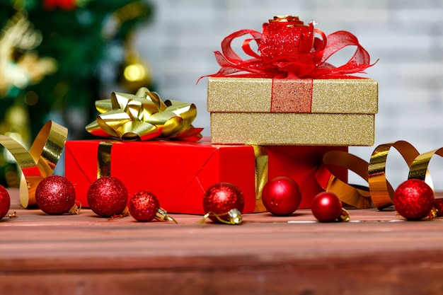 Colorful present gift boxes with bright color ribbon bow tie placed on corner of wooden table in front fully decorative beautiful Christmas eve pine tree and brick wall in blurred background.