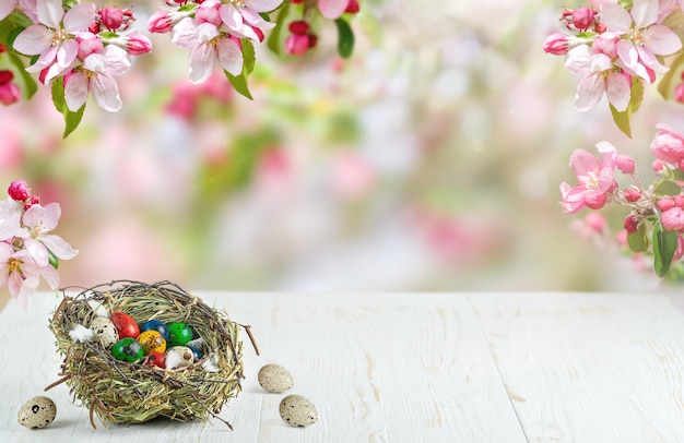 Colorful quail Easter eggs in nest on white wooden table on blurred floral bakground. Copy space. High quality photo