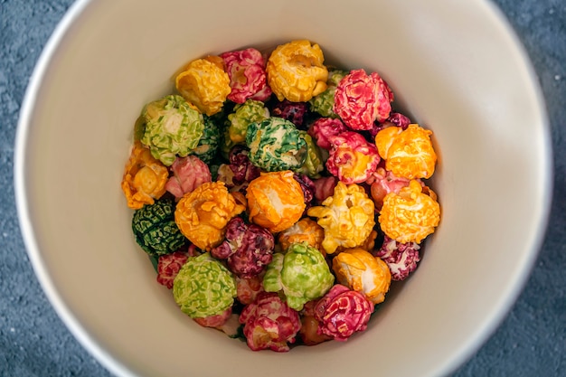 Foto popcorn di caramelle al caramello arcobaleno colorato su sfondo scuro. concetto di spuntino cinematografico. cibo per guardare film e intrattenimento. copia spazio per il testo, piatto.