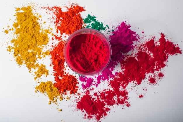 Colorful red holi powder in a glass bowl on white background and multicolored holi powder around it