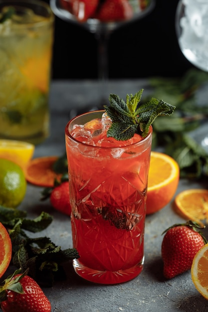 Colorful refreshing drinks for summer, cold strawberry lemonade juice with ice cubes in the glasses garnished with sliced fresh lemons.