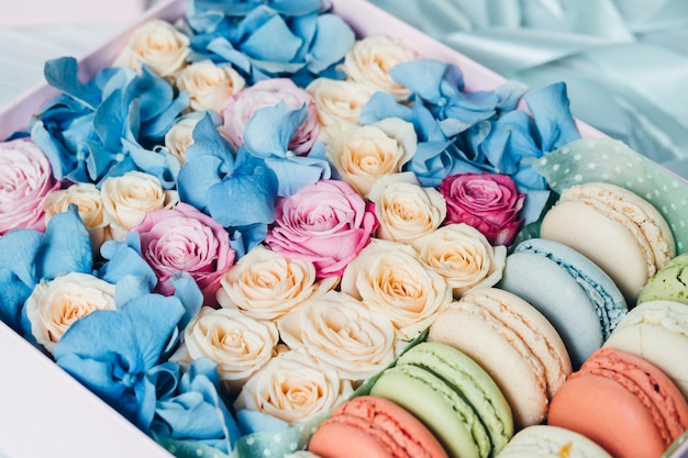 Разноцветные розы и макароны в розовой коробке на столе