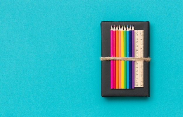 Красочные школьные и офисные принадлежности карандаши и линейка на черной книге и синем фоне