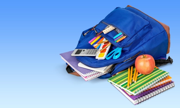 Colorful school supplies in backpack on blue background