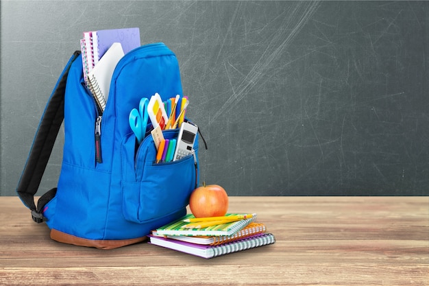 Colorful school supplies in backpack on wooden background