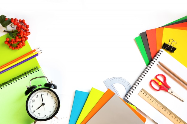 Colorful school supplies, book, and alarm clock on white.