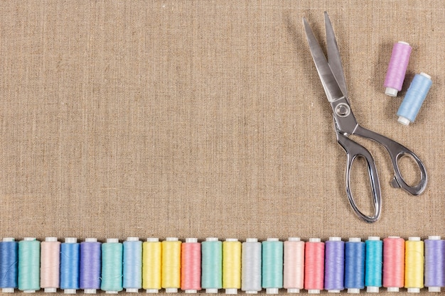 Colorful sewing threads and scissors on rough linen fabric with copy space Sewing tools top view