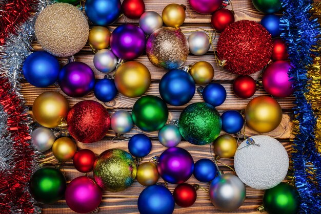 Colorful shiny Christmas balls and tinsel on wooden table background. Close-up view of Xmas holiday decoration. Beautiful still-life of flat lay festive composition for Happy New Year.