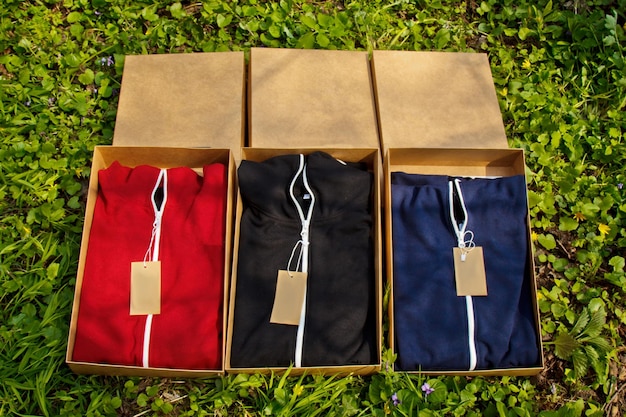마분지 상자에 접힌 태그가 있는 다채로운 운동복은 잔디 포장된 옷 꼭대기에서 포장 풀기 구매와 함께 바닥에 놓여 있습니다.