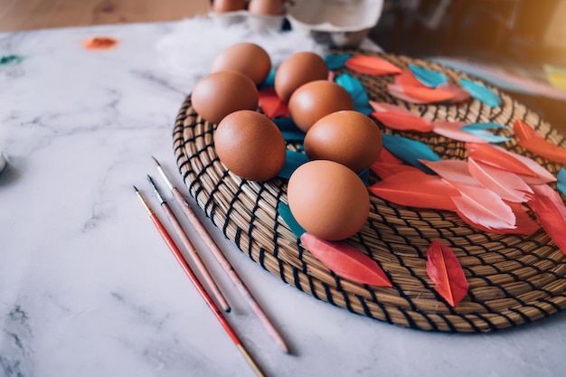 Colorful spring easter background with colored pink eggs, white feathers, dyes, brushes on light marble table. Copy space, top view. Happy Easter concept.