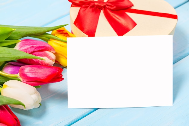 Colorful spring tulip flowers with decorative giftbox and blank  on light blue   