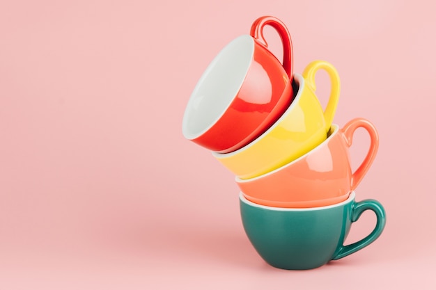 Colorful stack of cups for latte coffee on pink background.