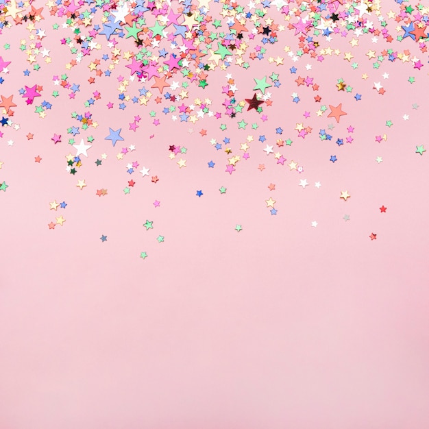 Photo colorful stars confetti on pink background with copy space