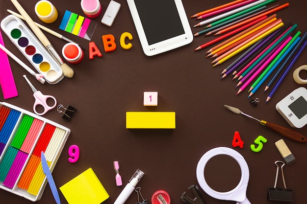 Photo colorful stationary school supplies on brown background, copyspace flat lay. school and office supplies frame