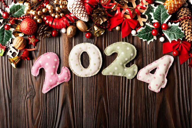 Фото Красочные сшитые цифры 2024 из ткани в горошек с рождественскими украшениями на плоском фоне на деревянном столе