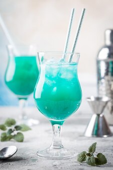 Cocktail estivo colorato blue hawaii o bevanda alcolica ghiacciata blu laguna con menta su sfondo di pietra chiara