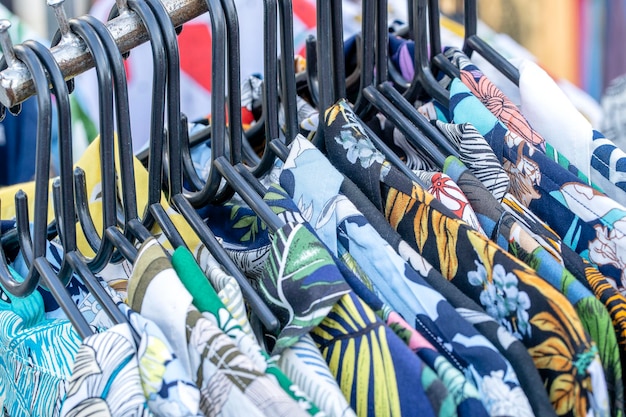 Colorful summer shirts on hangers for sale in street market in Thailand close up