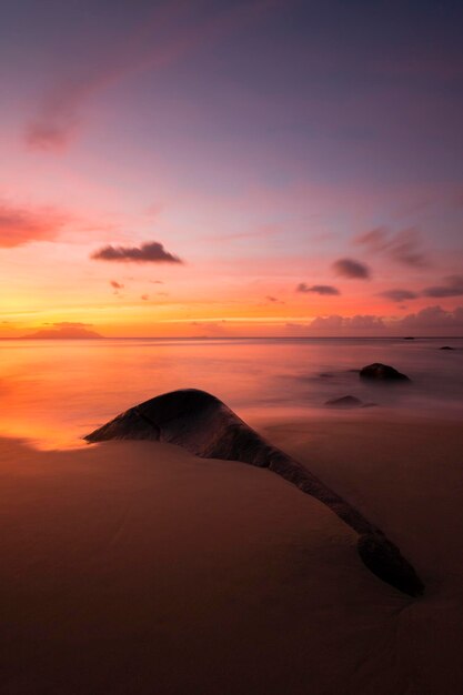 A colorful sunset over a beach with a large rock in the foreground