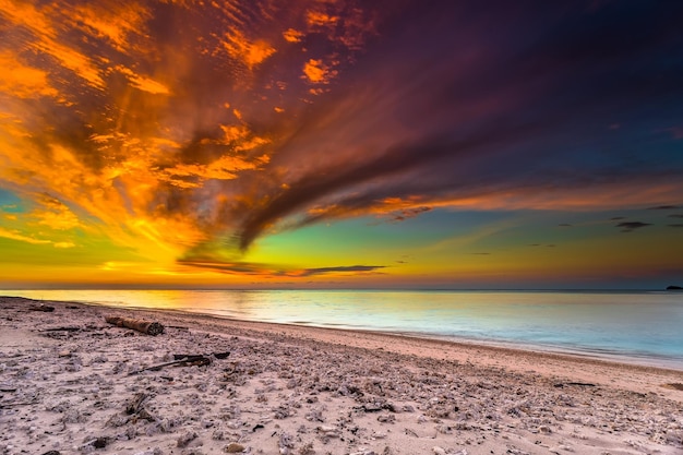 A colorful sunset over the ocean with a beach in the foreground.