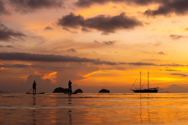 Colorful sunset on a tropical beach. Orange sunset on the ocean. Colorful sunset in the tropics. A pair of people are swimming on sup boards