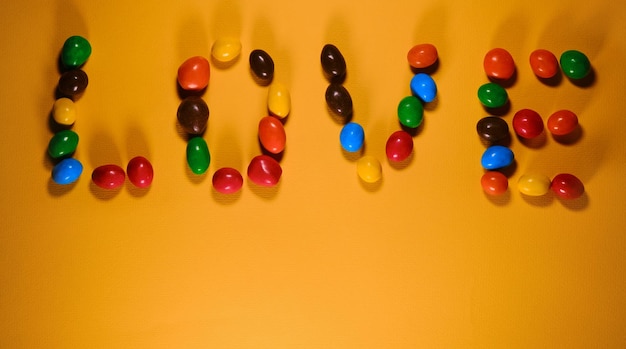 Colorful sweet candies lined with letters with inscription love on Yellow