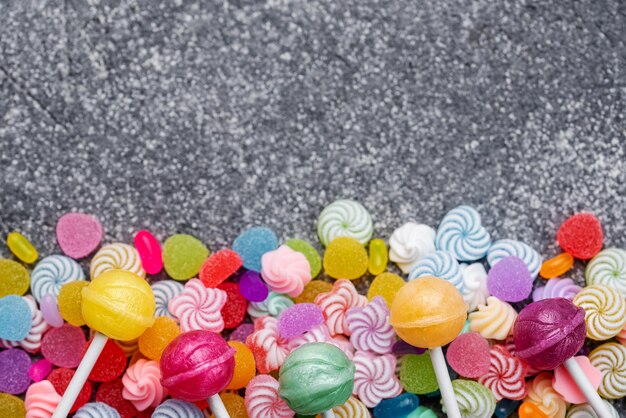 Colorful sweet lollipops and candies over black concrete background Flat lay top view