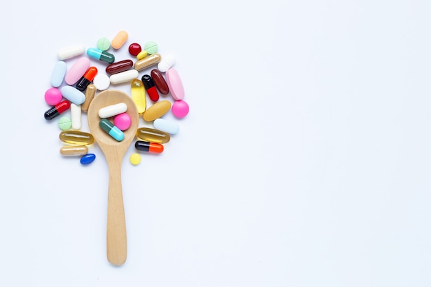 Colorful tablets, capsules and pills with wooden spoon on white