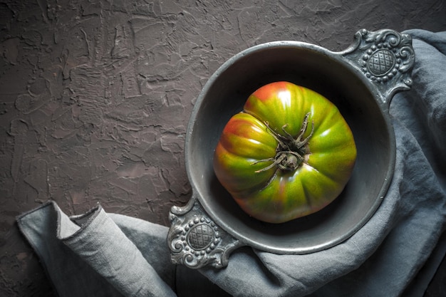 Colorful tomato in a tin bowl on a gray napkin