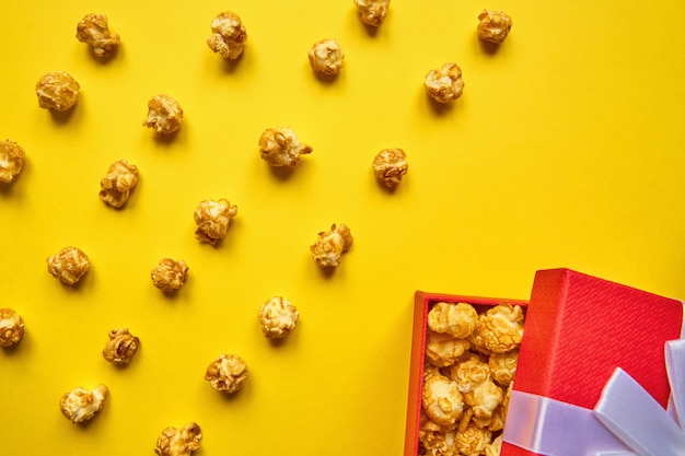 Foto sfondo colorato alla moda con popcorn al caramello e confezione regalo rosso su sfondo giallo