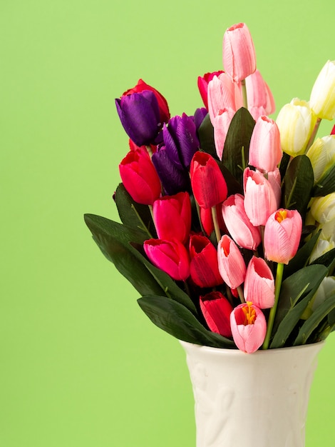 Фото Красочные тюльпаны в вазе на белом фоне стены зеленого стола