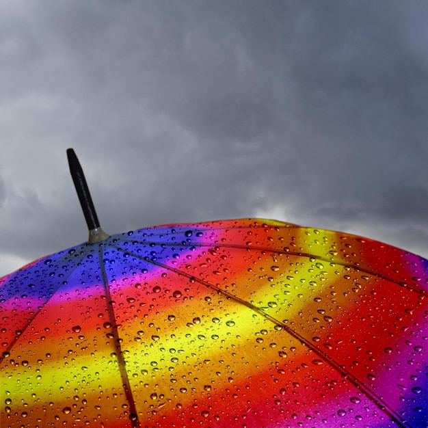 Foto parte superiore dell'ombrello colorato con gocce di pioggia e nuvole pesanti