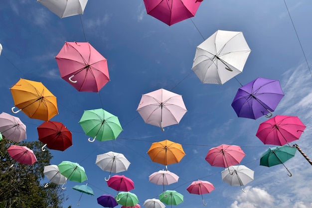 Photo colorful umbrellas are hanging from  wire with blue sky cloud in background