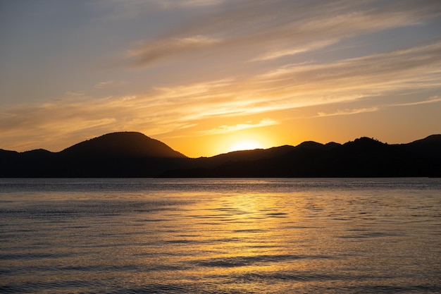 海と山の夕焼け空のオレンジ色のカラフルな景色水に沈む夕日の反射