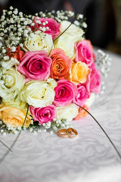 Красочный свадебный букет из роз лежит перед кольцами на столе